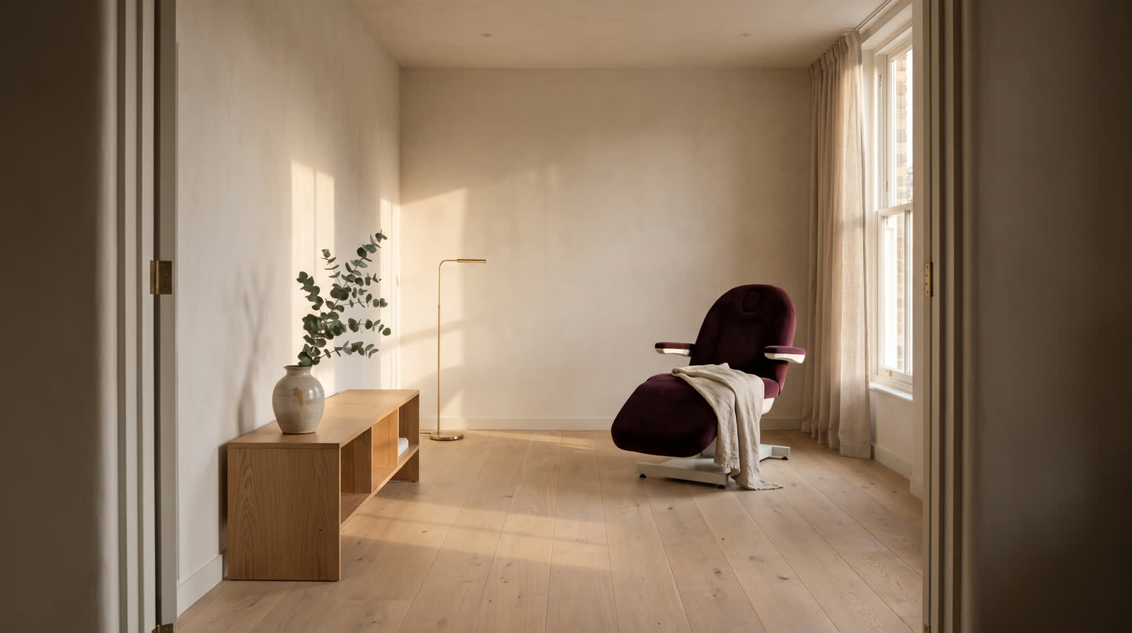 Sala de atendimento com parede clara, piso de madeira, poltrona vinho e janela alta